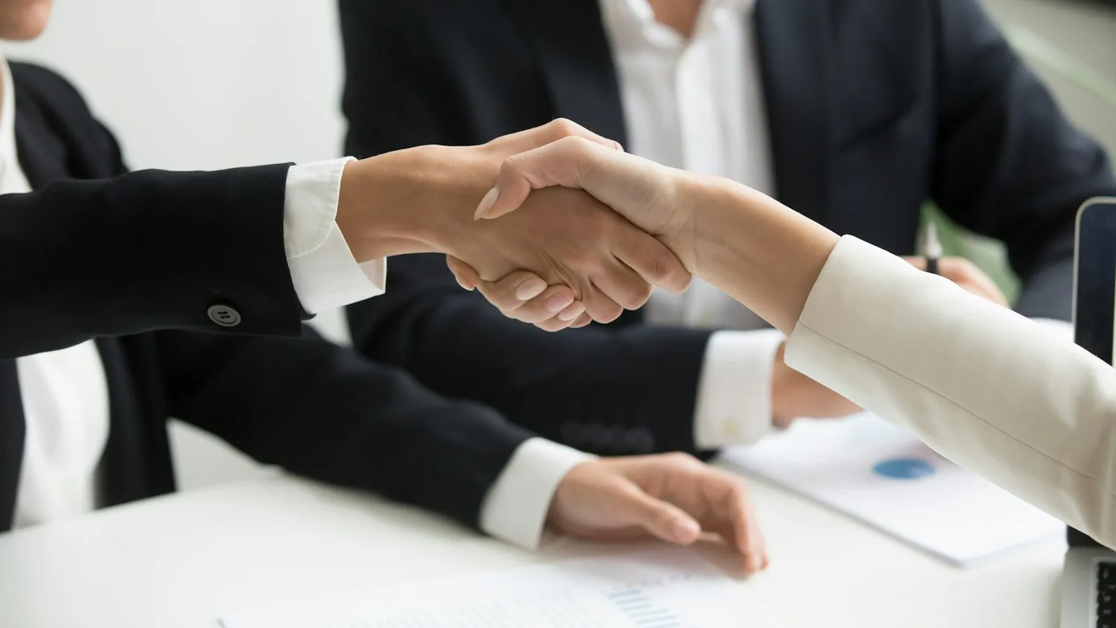 Zwei Geschäftspartner geben sich am Besprechungstisch die Hand, Sinnbild für die vorher vereinbarte Abrechnung per Gutschrift zwischen Auftraggeber und Vermittler