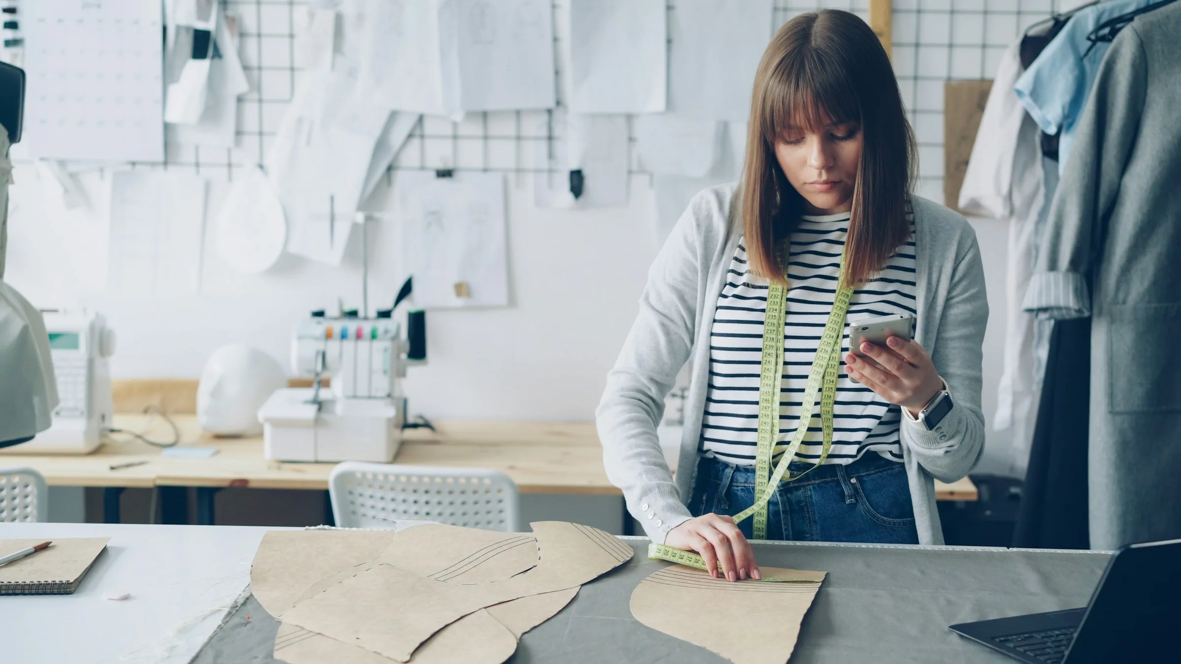Schneiderin vermisst Schnittmuster in ihrem Atelier und schaut aufs Smartphone