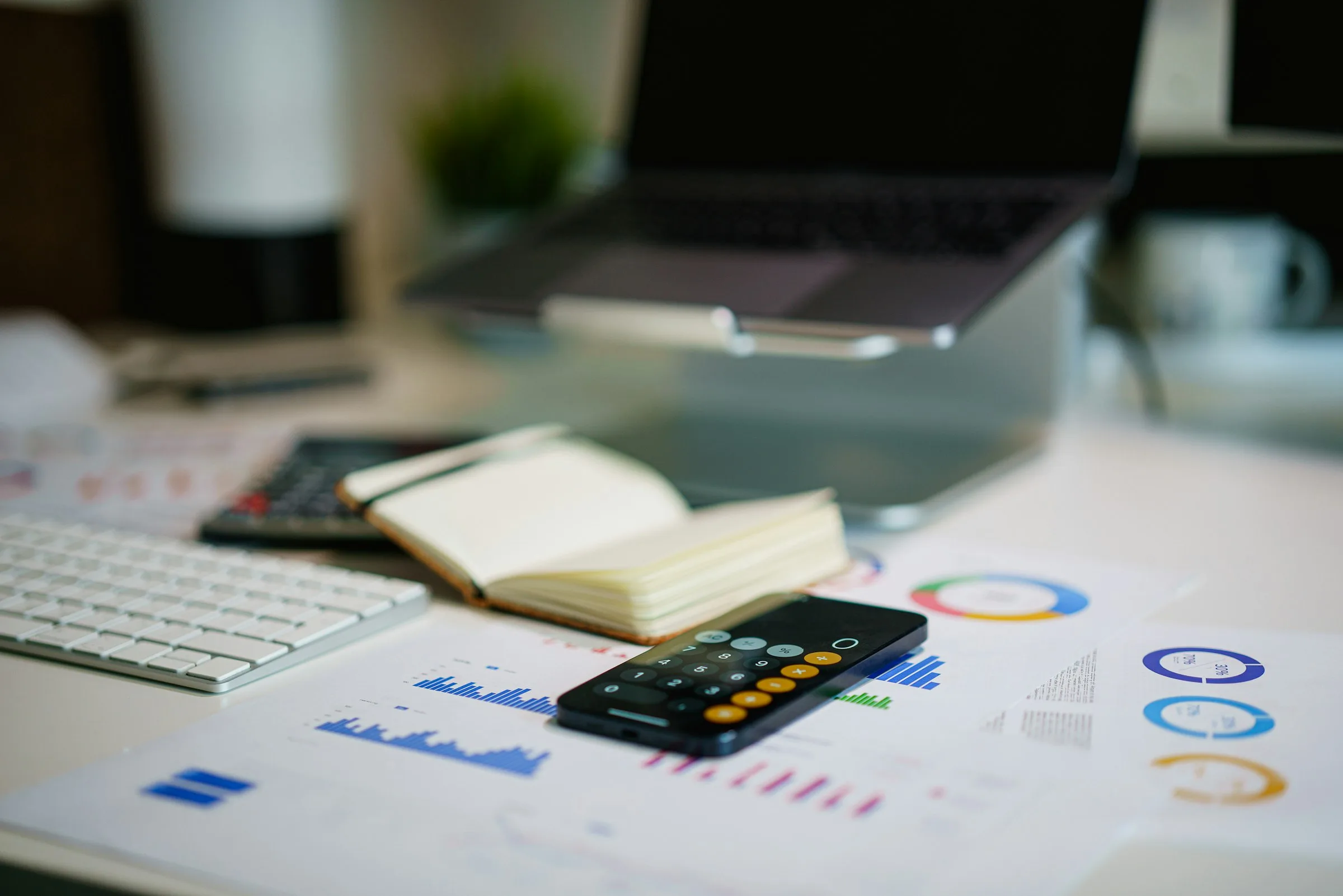 Schreibtisch mit Laptop, Smartphone-Taschenrechner und ausgedruckten Diagrammen