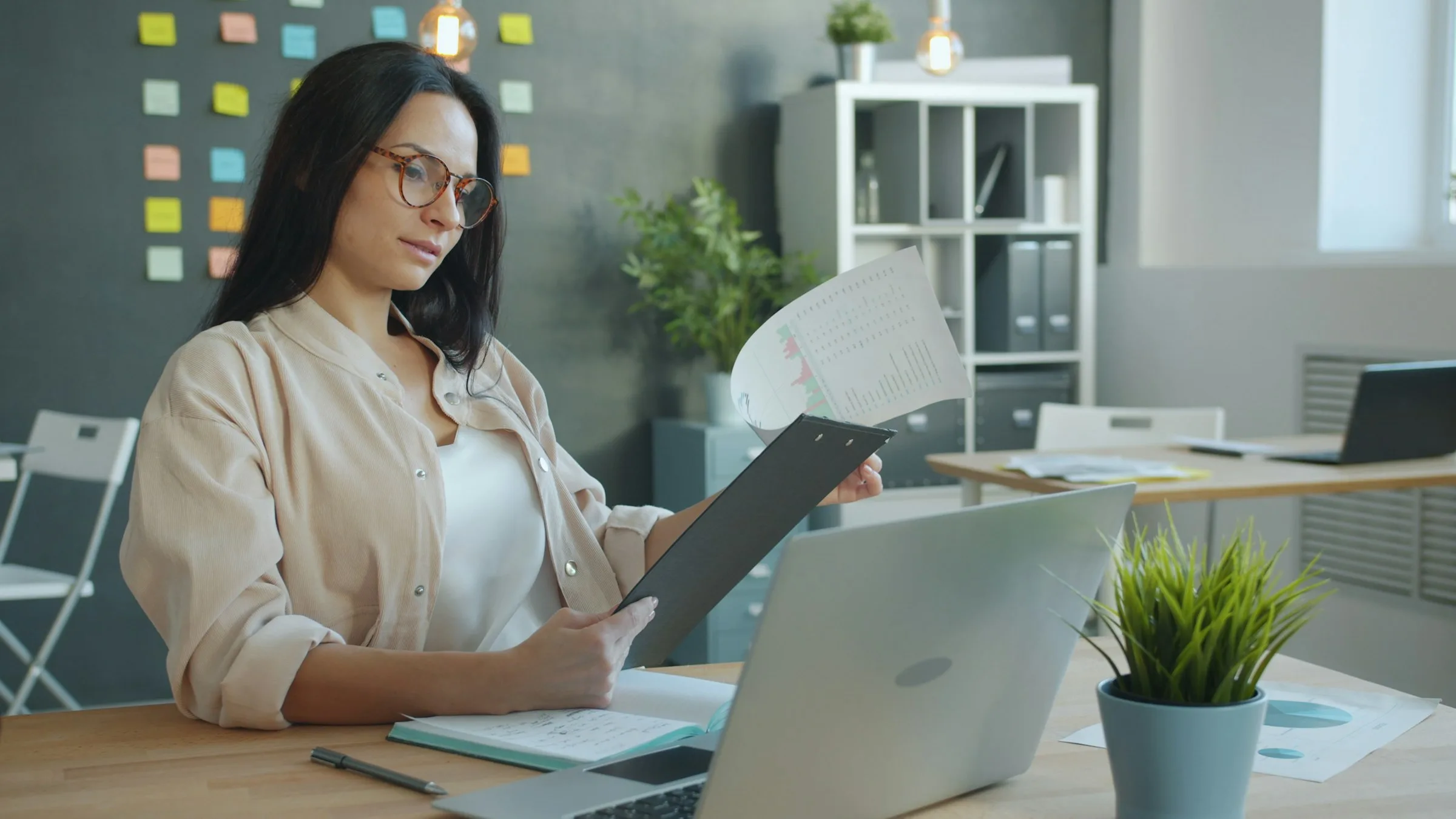 Frau hält eine Auswertung mit Diagrammen vor einem geöffneten Laptop